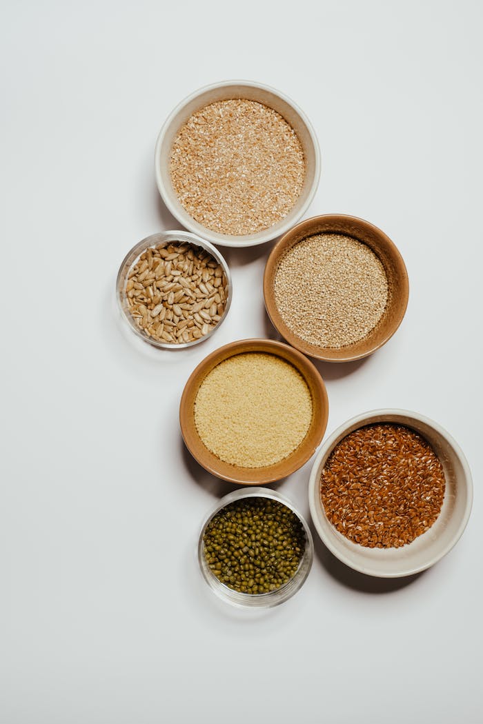 Top view of various seeds and grains displayed in ceramic bowls on a white background.