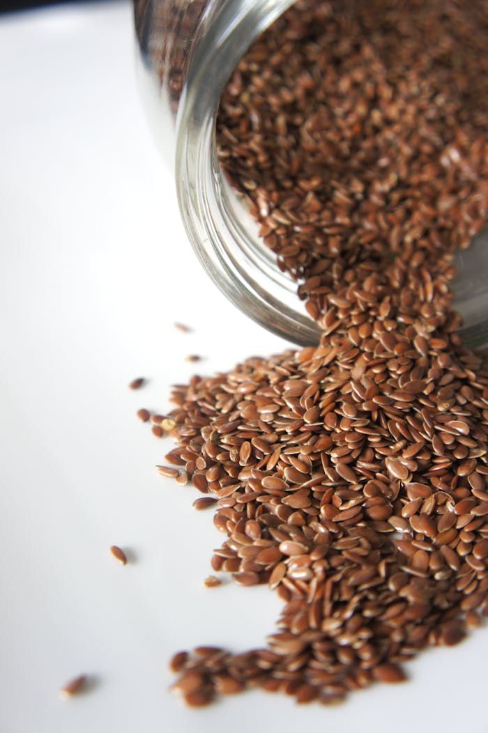 High angle view of flaxseeds spilling from a jar onto a white surface. Perfect for health and food concepts.